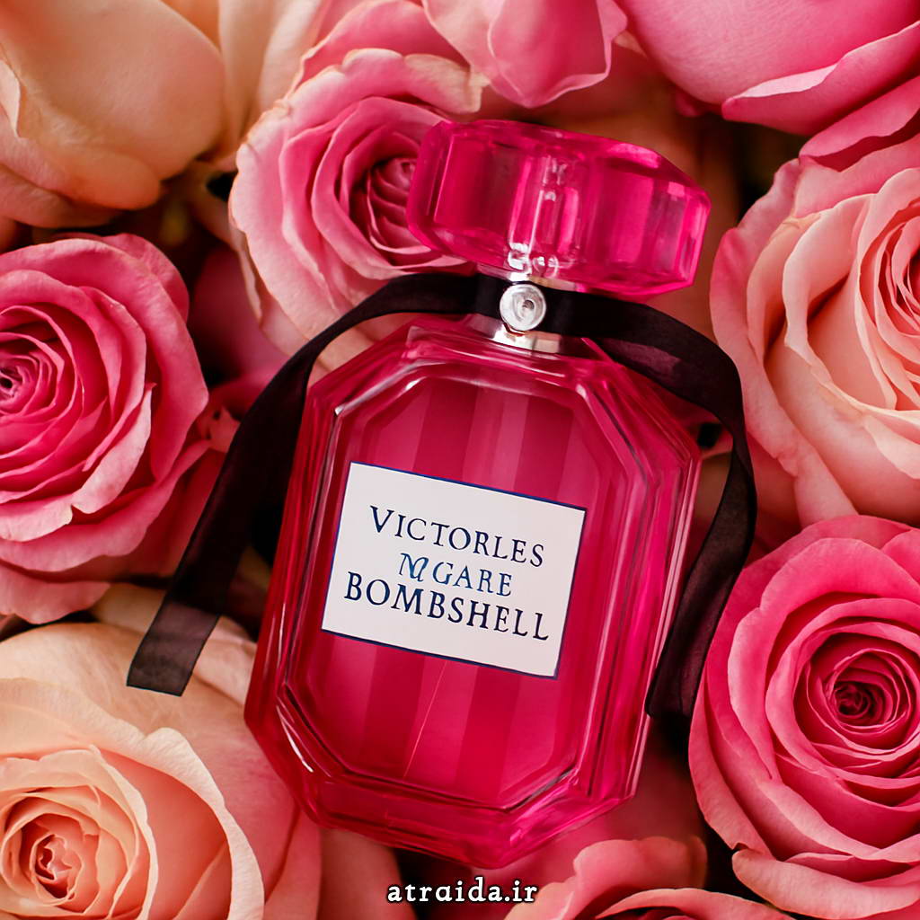 تصویر عطر ویکتوریا سکرت بامب شل "Bombshell" برند ویکتوریا سکرت در میان گل‌های رز صورتی و کرم که حس لطافت، زنانگی و جذابیت را القا می‌کند. برچسب "atraida.ir" عطر آیدا ( امیر عطری ) در پایین تصویر است